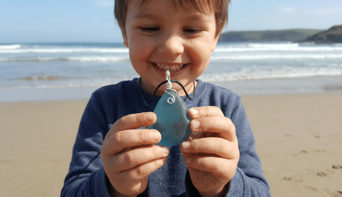 A hand holding a teardrop-shaped blue sea glass pendant wrapped in silver wire.